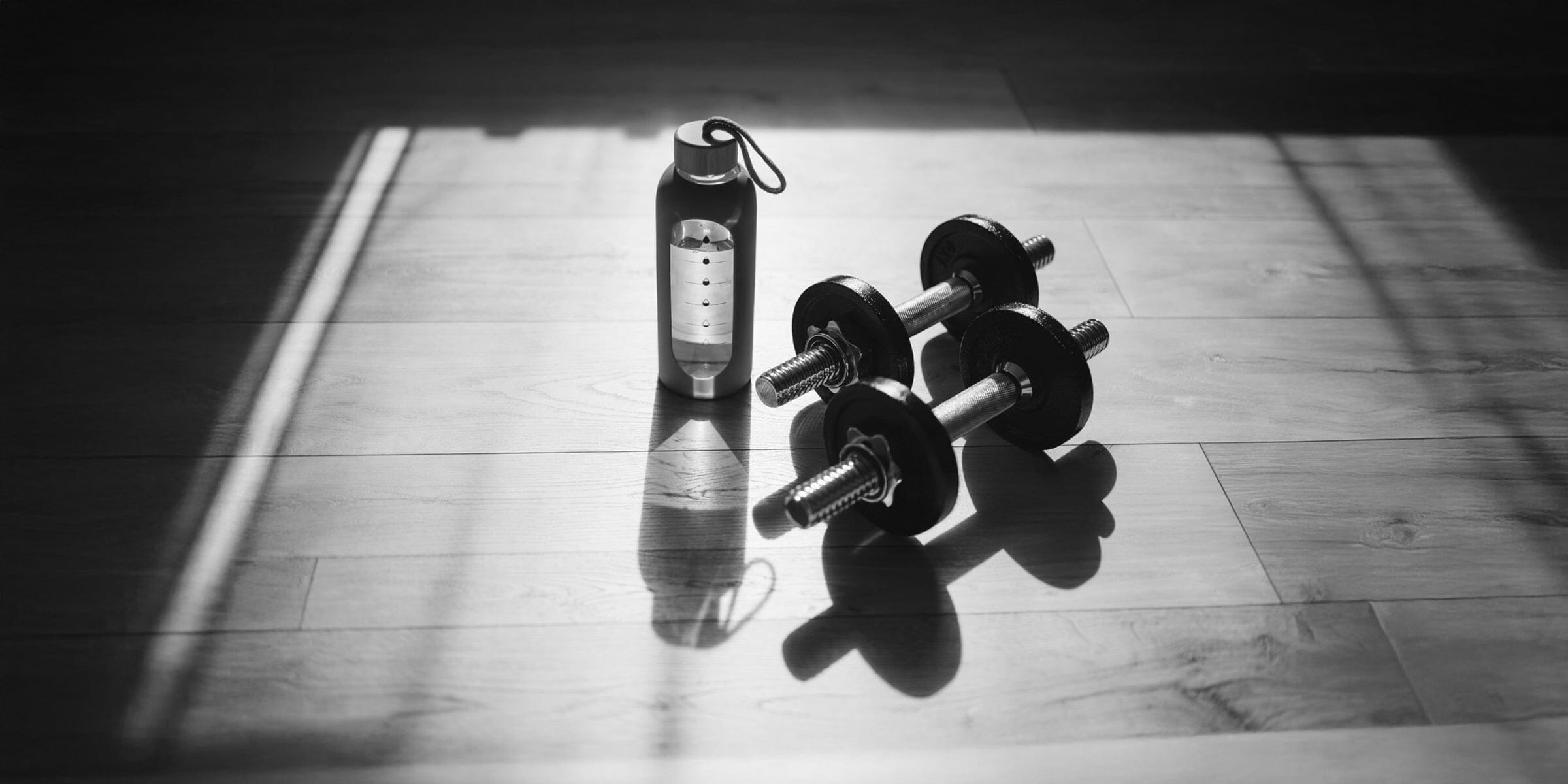 Shaker bottle of mixed micronized creatine next to dumbbells in a gym.